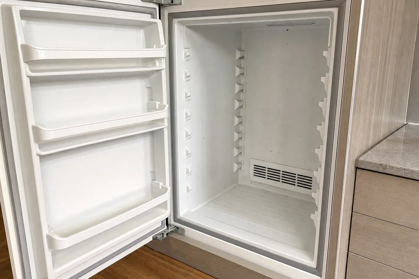 Interior of a built-in refrigerator column standing open and empty, door bins on the left and a rear vent grille
