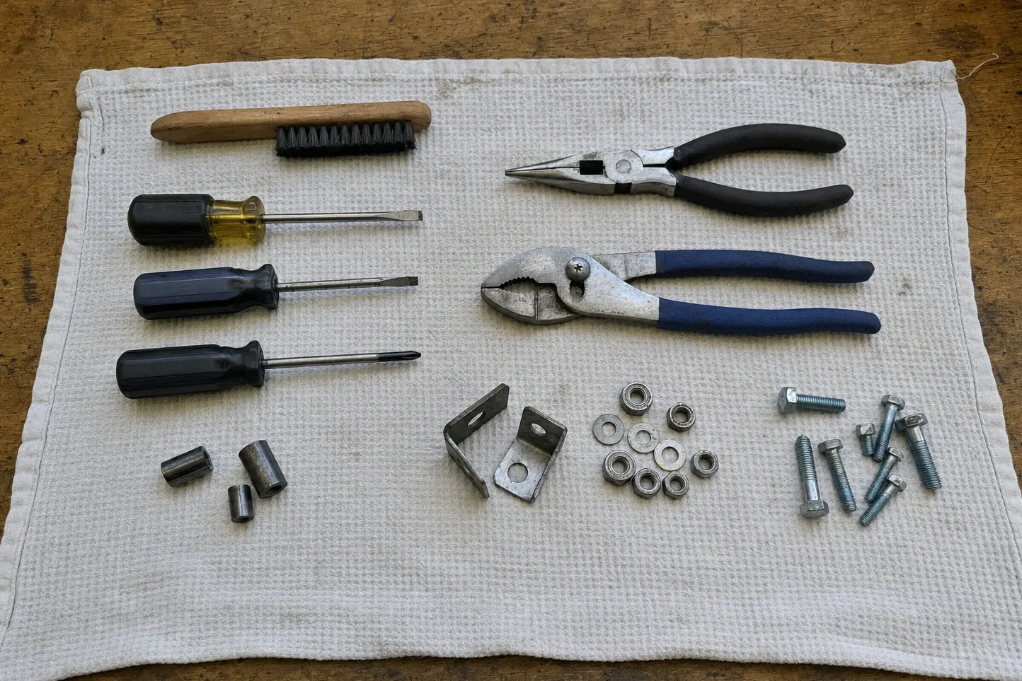 Three steel spacer sleeves, two angle brackets, nuts, washers and hex bolts laid in rows with a brush, drivers and two pairs of pliers